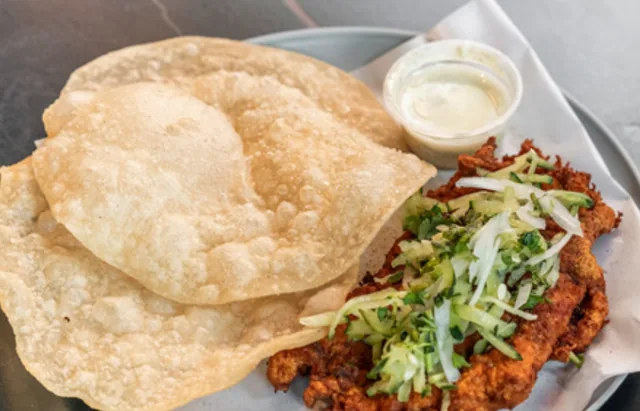 Chicken chap topped with shredded cucumber and cabbage, served with puffed luchi and a creamy dip