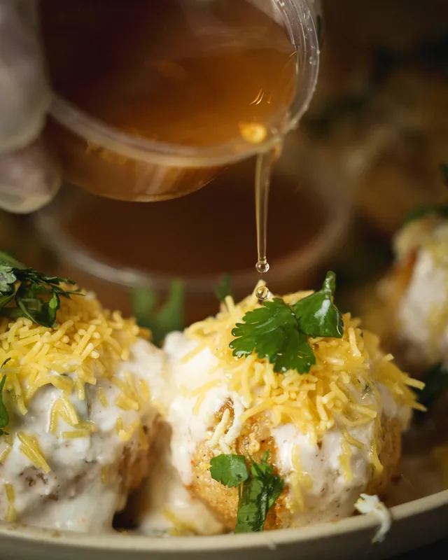 Tamarind water poured over doi fuchka topped with yogurt, crispy sev and cilantro