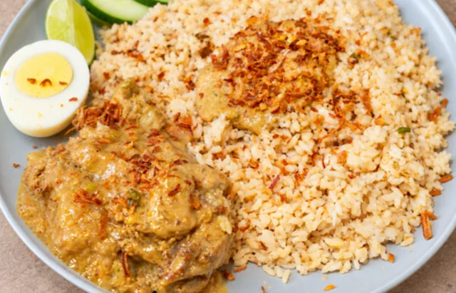 Morog polau: chicken in a rich gravy beside fragrant polao rice topped with fried onions, with a boiled egg, lime and cucumber
