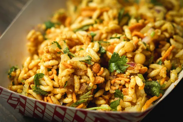 A paper boat of spiced puffed rice tossed with chickpeas, carrot, onion and cilantro