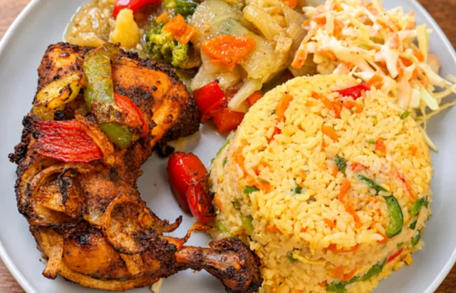 A tandoori chicken leg quarter with peppers and onions beside fried rice, mixed vegetables and coleslaw