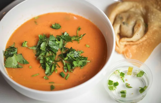 A bowl of Thai soup garnished with cilantro, with a wonton and a small cup of dip on the side